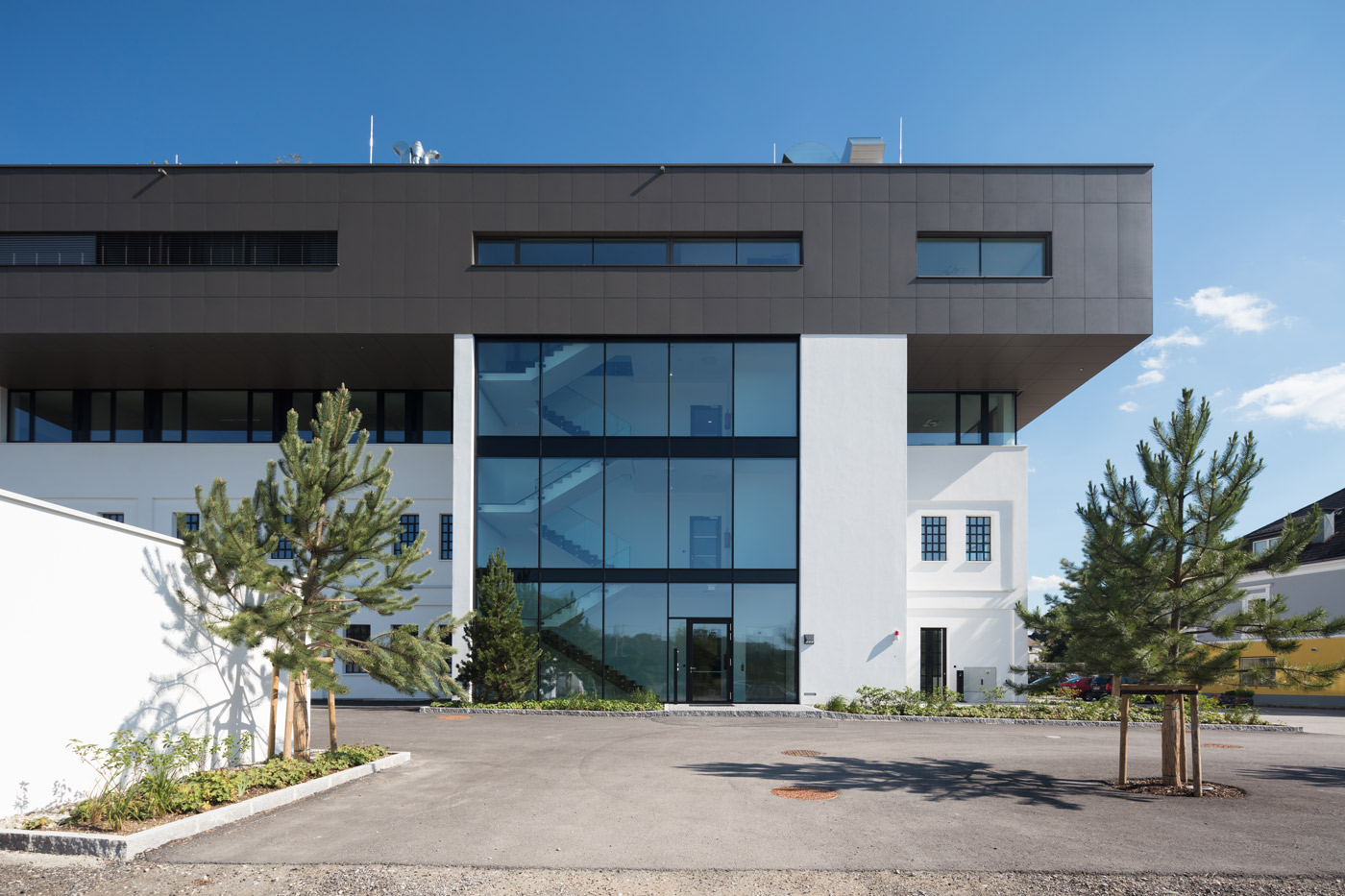 Die Federnfabrik von außen: weißer Altbau mit dunklem, auskragendem Aufbau und verglastem Stiegenhaus